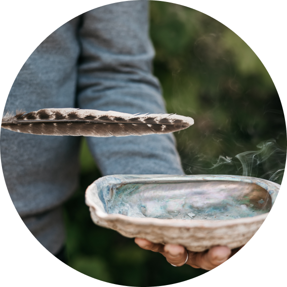 A hand holding a feather and Abalone shell in the process of smudging.